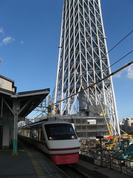 脇で東京スカイツリーの建設が進む業平橋駅と通過する200系特急「りょうもう」